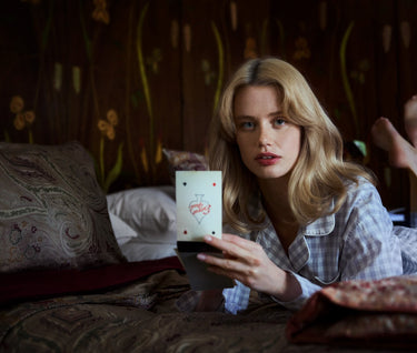 Woman wearing pajamas and a blackwatch plaid robe sitting at a table with gift wrapping supplies and chocolates.