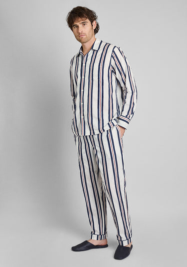 A man wearing white pajamas with navy and red stripes in front of a plain background. 