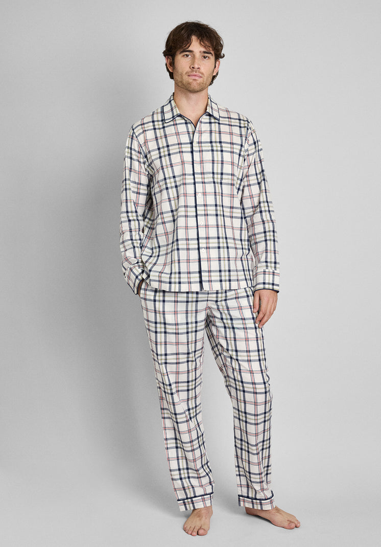 A man wearing a cream pajama set with a red, blue, and yellow madras print stands in front of a plain background. 
