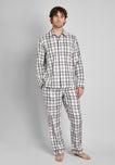 A man wearing a cream pajama set with a red, blue, and yellow madras print stands in front of a plain background. 