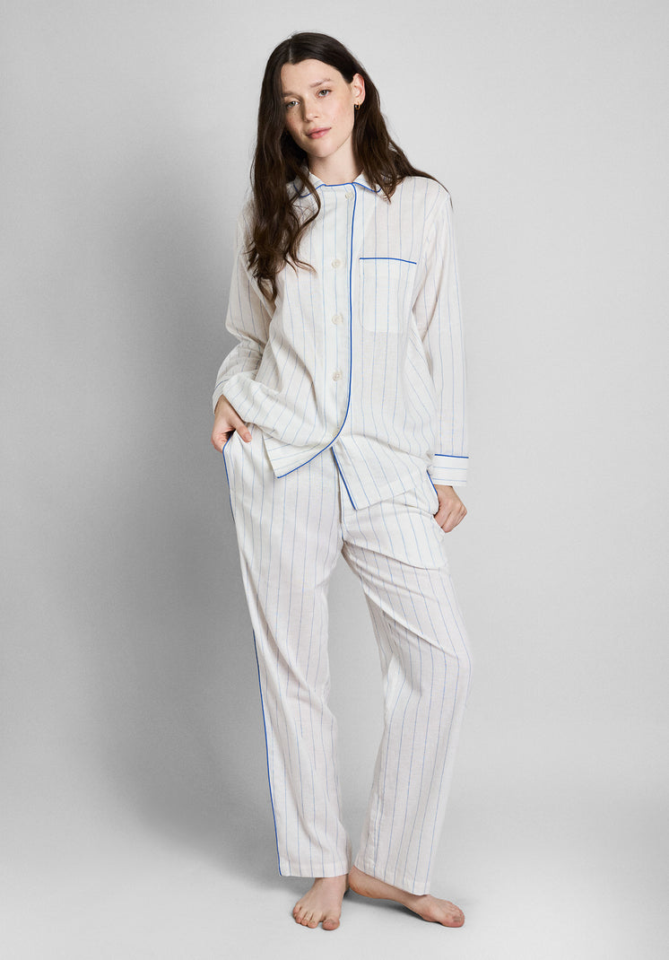 A woman wearing the Margaret Linen Pajama set, a white linen long sleeve and pants pajama set with blue stripes, blue piping details. Also features a chest pocket.