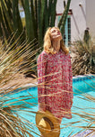Woman in a red floral nightdress standing by a pool with cacti and a building in the background